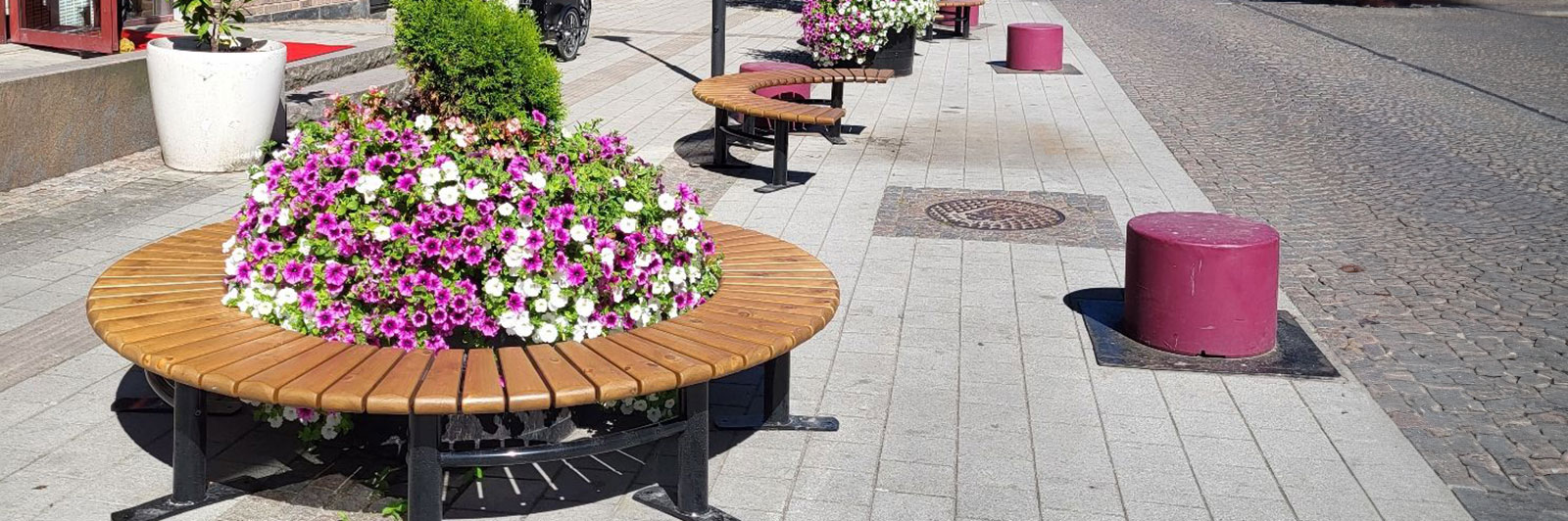 Modulære sittebenker formet som en sirkel rundt en stor blomsterpotte i midten.